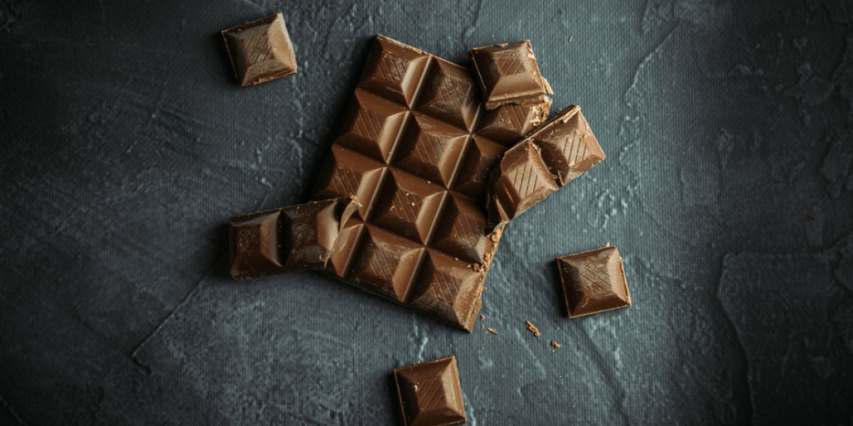 Eine Tafel Schokolade liegt auf dem Tisch mit Stückchen drum herum